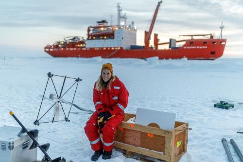 Friederike Krger auf einer Eisscholle im roten, warmen Schneeanzug, im Hintergrund ist das Begleitschiff "Akademik Fedorov" zu sehen.  Quelle: Mario Hoppmann